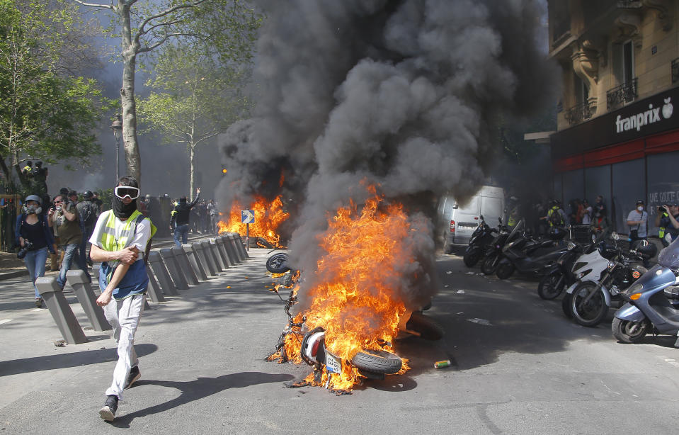 Un hombre corre junto a una motocicleta en llamas durante una protesta de chalecos amarillos en París, el sábado 20 de abril de 2019. (Foto AP/Michel Euler)