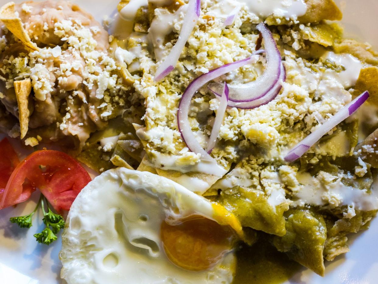 Delicious traditional Mexican breakfast picture. The picture shows green chilaquiles with cream, cotija cheese and onions accompanied with a fried egg and mashed beans with cheese and toots (tortilla chips).