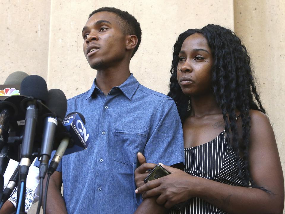 Dravon Ames, left, answers a question as Iesha Harper, right, joins her fiancee during a news conference at Phoenix City Hall, Monday, June 17, 2019, in Phoenix. Ames and his pregnant fiancée, Harper, who had guns aimed at them by Phoenix police during a response to a shoplifting report, say they don't accept the apologies of the city's police chief and mayor and want the officers involved to be fired. (AP Photo/Ross D. Franklin)