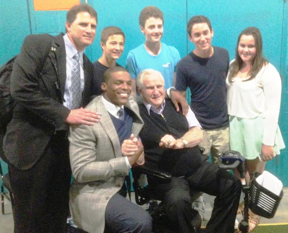 In 2013, after the Carolina Panthers edged the Miami Dolphins in Florida, quarterback Cam Newton (seated, left) and former NFL head coach Don Shula posed for a photo, surrounded by members of Shula’s family. Mike Shula, the Panthers’ offensive coordinator at the time, is standing on the far left.