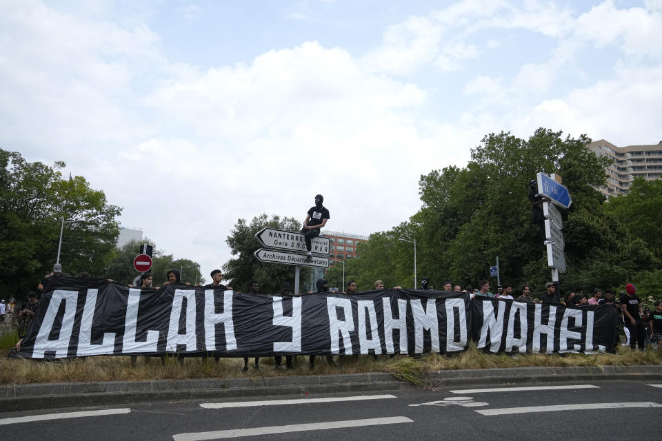 FILE - A man sits on a road sign above a banner reading "Allah, mercy for Nahel" during a march for Nahel, Thursday, June 29, 2023 in Nanterre, outside Paris. Officially, race doesn't exist in France. But the killing of the French-born 17-year-old with North African roots has again exposed deep feelings about systemic racism that lie under the surface of the country's ideal of color-blind equality. (AP Photo/Michel Euler, File)