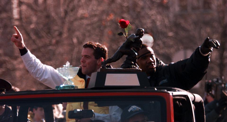 Brian Griese, with the Rose Bowl MVP trophy, and Charles Woodson, with the Heisman, ride in a Jeep and wave to the crowds gathered on State St. during the celebration parade for the University of Michigan football team in 1997 in Ann Arbor.