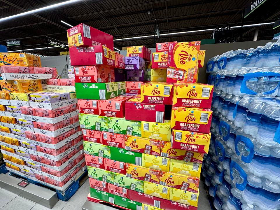 Boxes of sparkling water at Aldi. Purple, yellow, and pink boxes of La Croix sit next to green, red, and yellow boxes of PurAqua Belle Vie water