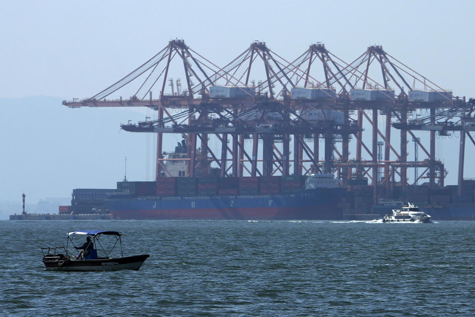 A man on a boat fishes as a ferry sails by a containers vessel docked at a port shrouded by haze in Xiamen in southeast China's Fujian province on Dec. 26, 2023. The United Nations issued a somber global economic forecast for 2024 on Thursday, Jan. 4, 2024, pointing to challenges from escalating conflicts, sluggish global trade, persistently high interest rates and increasing climate disasters. (AP Photo/Andy Wong)