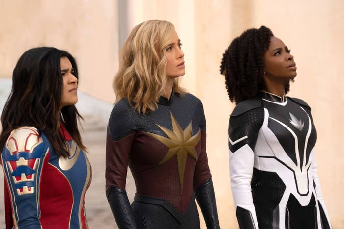 Iman Vellani, Brie Larson, and Teyonah Parris in superhero costumes from the Marvel film "The Marvels," looking upwards