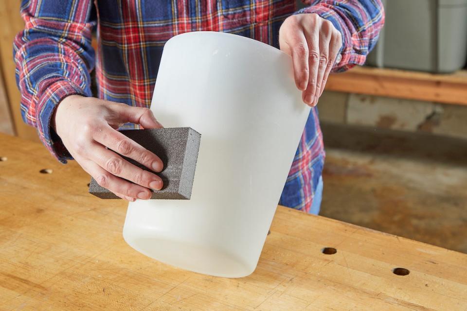 Woman using sandpaper to sand a plastic bin.