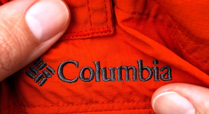 An image with two thumbs stretching out a black stitched "Columbia" logo on a red piece of clothing.