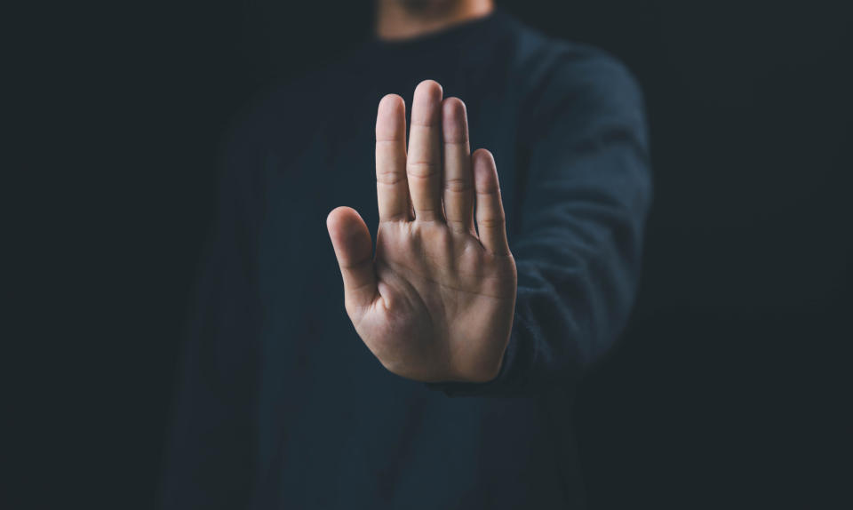 A person's outstretched hand facing forward, suggesting a "stop" or "no" gesture, against a dark background