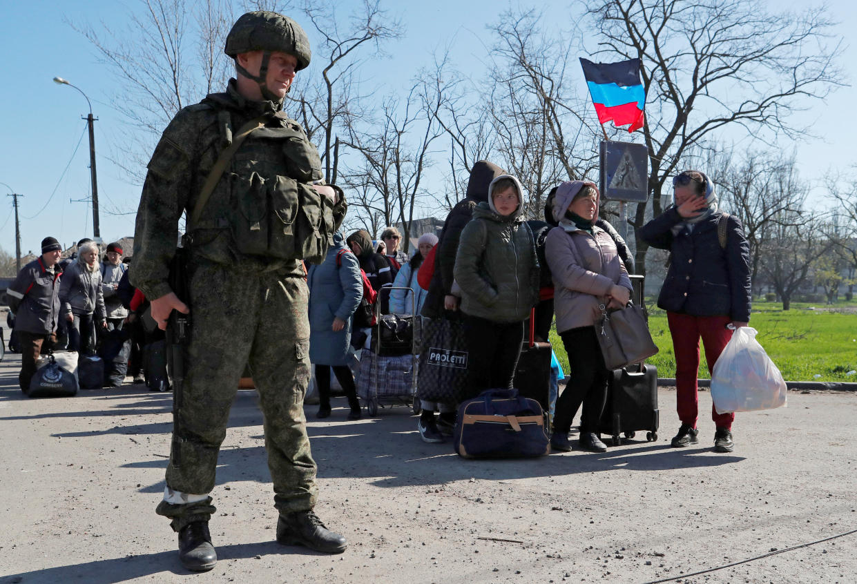 A pro-Russian service member stands guard as evacuees wait to board a bus in Mariupol.