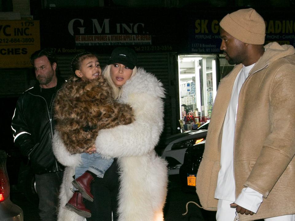 kanye west, kim kardashian, and a very young north west photographed on the street in new yokr. in the background, behind kim holding north, bodyguard steve stanulis stands, looking over to the side.