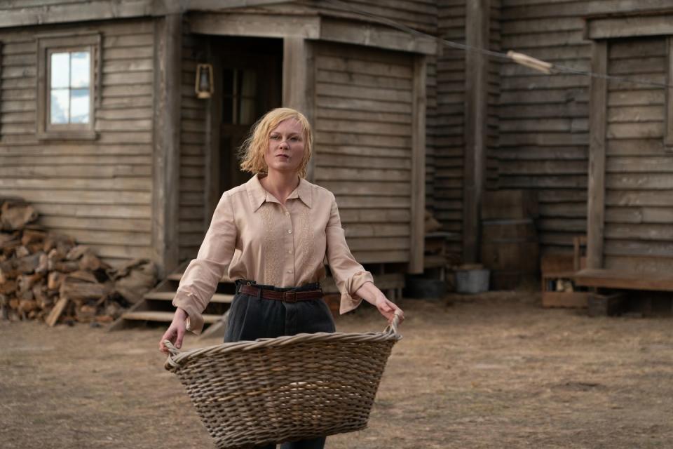 kirsten dunst holding a basket as she walks in front of a house in a scene from a movie