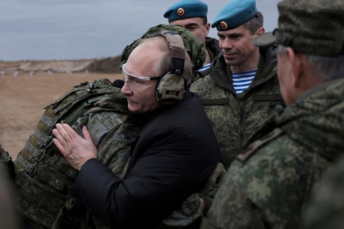 Russian President Vladimir Putin, wearing eye and ear protection and a black coat, hugs a soldier outdoors