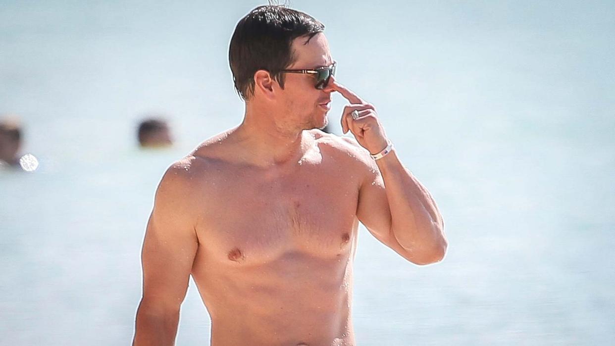  Mark Wahlberg walking on beach with sunglasses . 