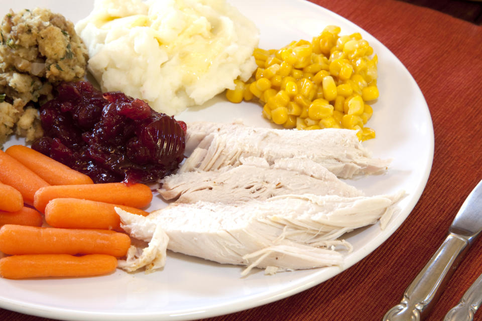 A plate with turkey slices, baby carrots, mashed potatoes, corn, stuffing, and cranberry sauce. A knife and fork are next to the plate