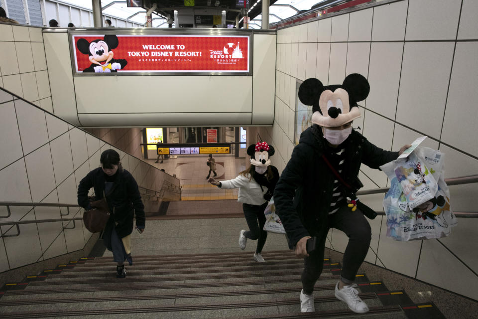 Two women rush to catch a train after visiting Tokyo Disneyland in Urayasu, near Tokyo, Feb. 28, 2020. The amusement park will be closed from Saturday until March 15 in an effort to prevent the spread of COVID-19. (AP Photo/Jae C. Hong)