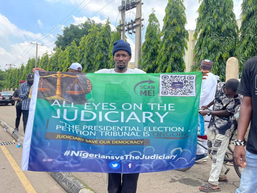 A man holds a banner that reads All eyes on the Judiciary on a street in Abuja Nigeria Wednesday , Sept. 6, 2023. Nigeria’s presidential tribunal will on Wednesday deliver its judgement on opposition challenges against the disputed election that produced Bola Tinubu as president of Africa’s most populous country, taking office 100 days ago. (AP Photo/Chinedu Asadu)