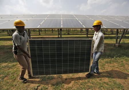 Workers carry a damaged photovoltaic panel inside a solar power plant in Gujarat, India, July 2, 2015. REUTERS/Amit Dave