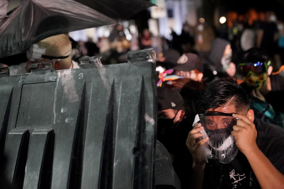 A protester takes cover during clashes outside the Kenosha County Courthouse late Tuesday, Aug. 25, 2020, in Kenosha, Wis. Protests continue following the police shooting of Jacob Blake two days earlier. (AP Photo/David Goldman)