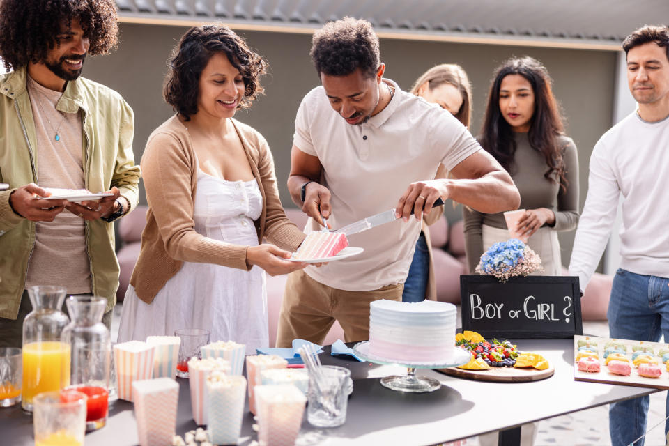 Group of people at a gender reveal party as a couple prepares to announce their baby's gender with a cake