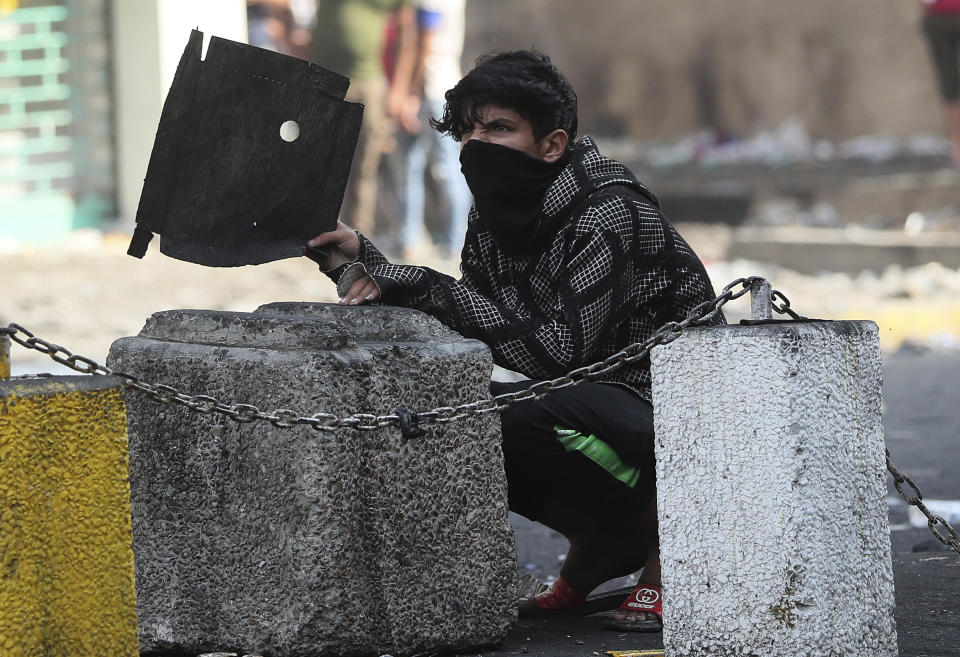 A protester takes cover during ongoing protests, in downtown Baghdad, Iraq, Wednesday, Nov. 13, 2019. (AP Photo/Hadi Mizban)