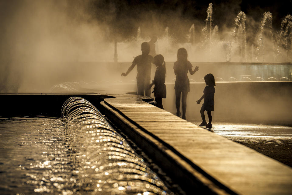 Children enjoy the drizzle from a public fountain before sunset in Bucharest, Romania, Thursday, June 20, 2024 as temperatures exceeded 38 degrees Celsius (100.4 Fahrenheit). The national weather forecaster issued a orange warning for western and southern Romania where temperatures are expected to reach 38 degrees Celsius (100.4 Fahrenheit) in the coming days. (AP Photo/Vadim Ghirda)