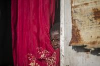 Jonelson Princeton, 7, who survived cholera as a newborn, peers out from inside his home which was once used as an office, on a former UN base where he lives with his parents and grandmother in Mirebalais, Haiti, Monday, Oct. 19, 2020. Ten years after a cholera epidemic swept through Haiti and killed thousands, families of victims still struggle financially and await compensation from the United Nations as many continue to drink from and bathe in a river that became ground zero for the waterborne disease. (AP Photo/Dieu Nalio Chery)