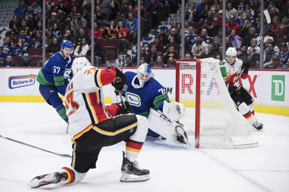 Calgary Flames' Sean Monahan, front, scores against Vancouver Canucks goalie Jacob Markstrom (25), of Sweden, as Canucks' Tyler Myers (57) and Flames' Johnny Gaudreau (13) watch during the third period of an NHL hockey game Saturday, Feb. 8, 2020, in Vancouver, British Columbia. (Darryl Dyck/The Canadian Press via AP)