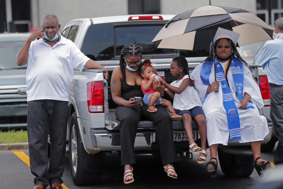 Daria Jones, graduate of New Orleans Charter Science and Math High School class of 2020, waits at their vehicle with her father Daryl Jones, left, sister Janeice Marchand and two nieces, during a drive-in graduation ceremony as a result of the COVID-19 pandemic, outside Delgado Community College in New Orleans, Wednesday, May 27, 2020. Students and family got out of their cars to receive diplomas one by one, and then held a parade of cars through city streets. (AP Photo/Gerald Herbert)