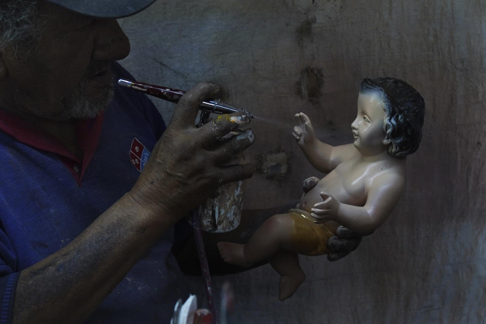 Un hombre pinta una figura del niño Dios restaurada en preparación para la fiesta del "Día de la Candelaria" en la Ciudad de México, el miércoles 25 de enero de 2023. (AP Foto/Marco Ugarte)