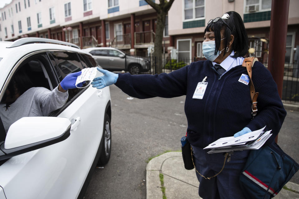 In this Wednesday, May 6, 2020, photo, Esther Haynes, left, gives United States Postal Service carrier Henrietta Dixon a protective face mask as she delivers mail along her route in Philadelphia. From coastal Maine to Philadelphia's close-knit neighborhoods, many residents call the postal service essential to their communities. (AP Photo/Matt Rourke)