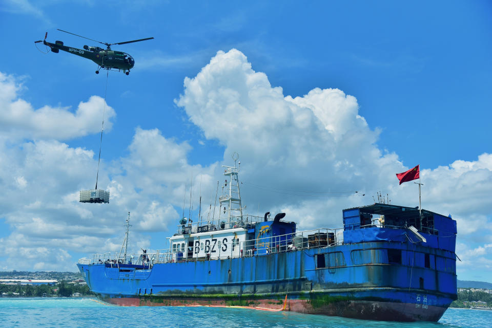 A helicopter drops cargo containing oil pumping equipment onto the deck of the FV Lu Rong Yuan Yu, a Chinese-flagged fishing vessel that has run aground, at Pointe-aux Sables, Port-Louis, Mauritius, Tuesday March 9 2021. Workers in Mauritius have begun pumping 130 tons of fuel from a Chinese fishing vessel that ran aground on a coral reef on the Indian Ocean island’s west coast on Sunday. Local newspaper L’Express reported that the grounded ship has spilled a small amount of fuel into the ocean, but its hull remains intact. (Beekash Roopun/L'express Maurice via AP)