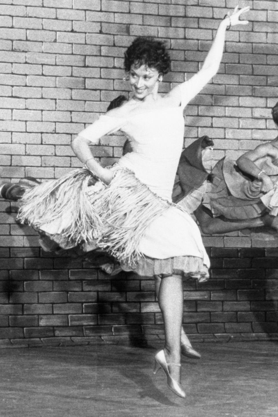 Four dancers in mid-performance with dynamic poses against a brick wall backdrop