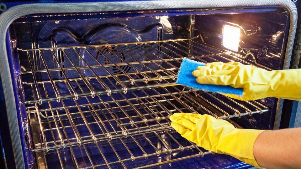 Gloved hands cleaning an oven in a kitchen.