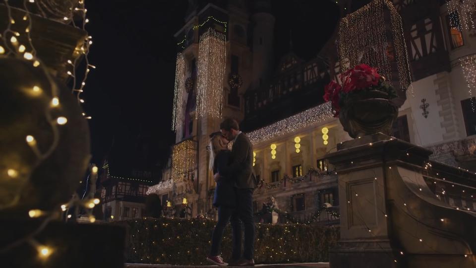 A man and a woman kiss in the garden of a castle.