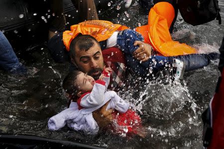 A Syrian refugee holds onto his children as he struggles to walk off a dinghy on the Greek island of Lesbos, after crossing a part of the Aegean Sea from Turkey to Lesbos September 24, 2015. REUTERS/Yannis Behrakis