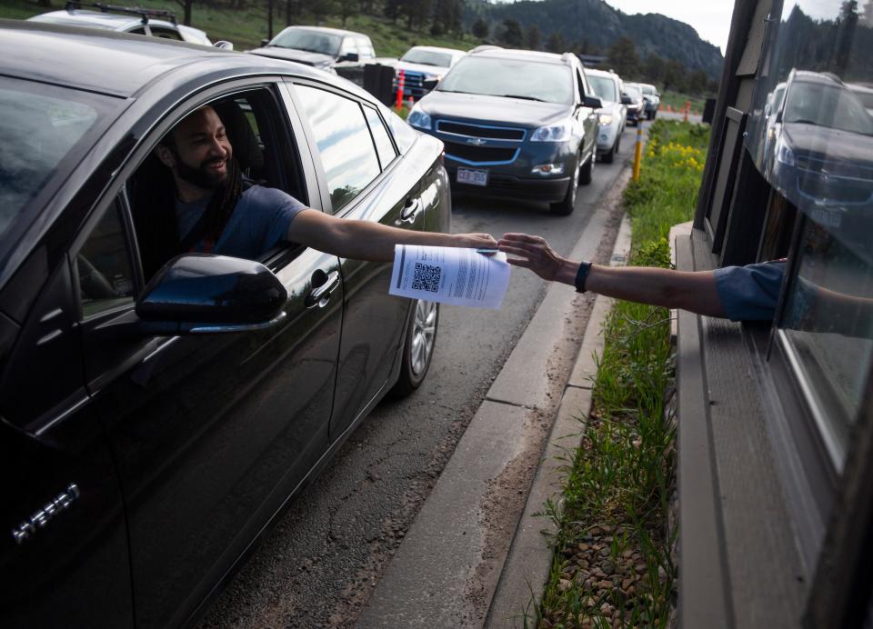 A man hands his timed-entry pass and driver's license to a park ranger at the entrance to Rocky Mountain National Park in Fort Collins, Colo.