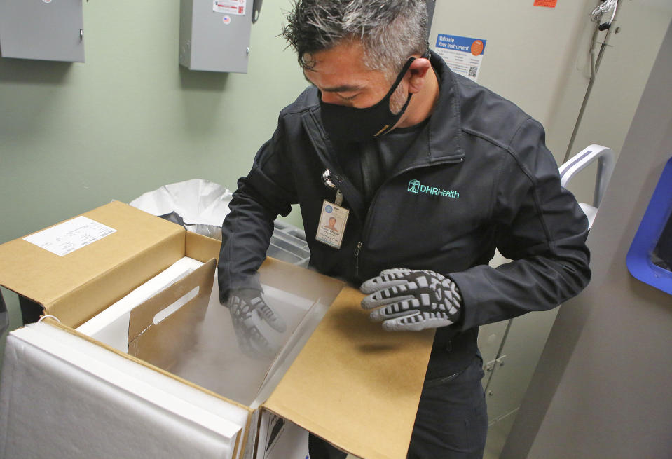 Gabriel Vasquez, pharmacy tech supervisor, reaches into the cold wearing gloves as he moves boxes of COVID-19 vaccines into a specialized freezer as they arrived at DHR Health on Tuesday, Dec. 15, 2020, in Edinburg, Texas. DHR Health received 5850 doses of the vaccine. (Joel Martinez/The Monitor via AP)