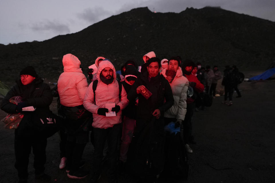 Asylum-seeking migrants hold their documents as they line up in a makeshift, mountainous campsite to be processed after crossing the border with Mexico, Friday, Feb. 2, 2024, near Jacumba Hot Springs, Calif. (AP Photo/Gregory Bull)