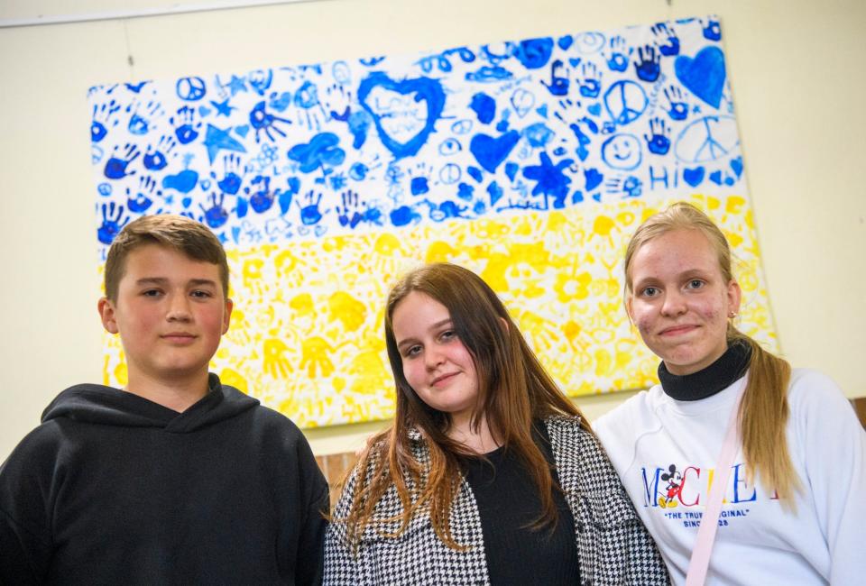 Ivan Kovalyov, left, Zlata Yadukha, middle, and Violetta Prsychepova pose under artwork representing the Ukrainian flag that Harmony School students made as a welcome on Tuesday, May 24, 2022.