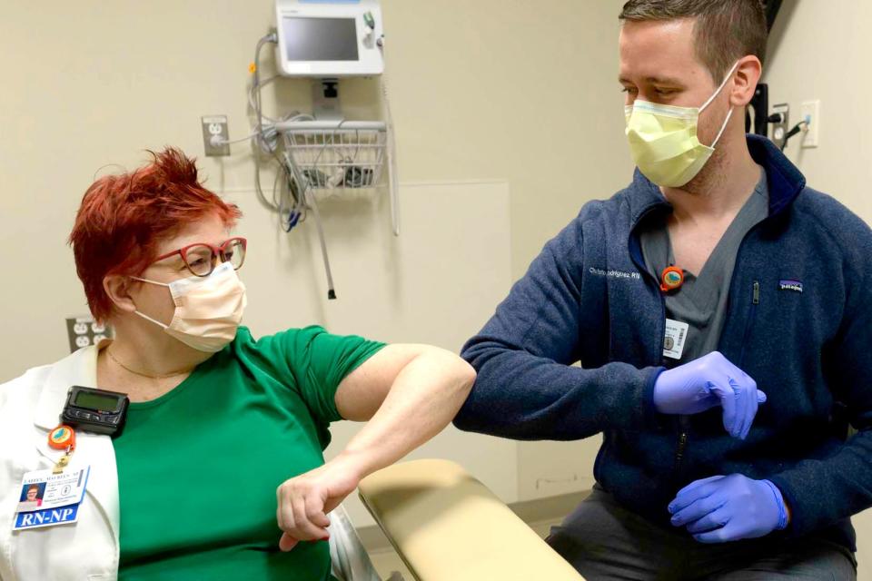 A nurse practitioner elbow-bumping a nurse after receiving a COVID-19 vaccine.