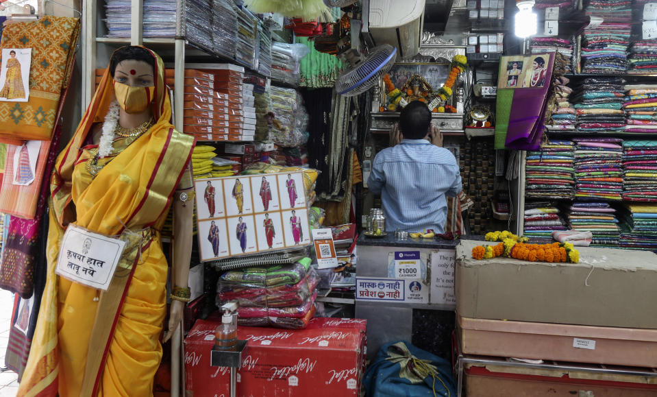 Signage in Marathi on a mannequin draped with a sari reads, "please don't touch" as a shopkeeper offers prayers before an image of Hindu deity Ganesh as he starts his day in Mumbai, India, Monday, June 7, 2021. . Businesses in two of India's largest cities, New Delhi and Mumbai, are reopening as part of a phased easing of lockdown measures in several states now that the number of new coronavirus infections in the country is on a steady decline. (AP Photo/ Rafiq Maqbool)