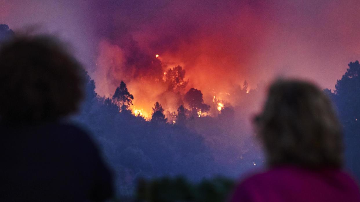 Two people in the foreground are stood with their backs to the camera watching wildfire spreading in a forest in Silvares, Portugal on Friday