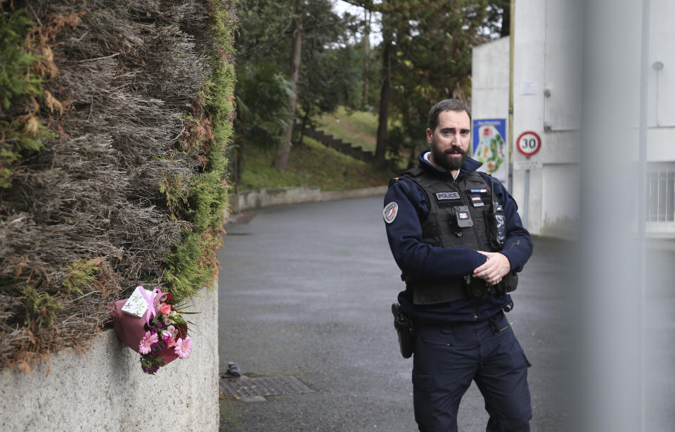 A police officer guards the entrance to a private Catholic school next to a bouquet of flowers after a teacher of Spanish has been stabbed to death by a high school student, Wednesday, Feb. 22, 2023 in Saint-Jean-de-Luz, southwestern France. The student has been arrested by police, the prosecutor of Bayonne said. (AP Photo/Bob Edme)