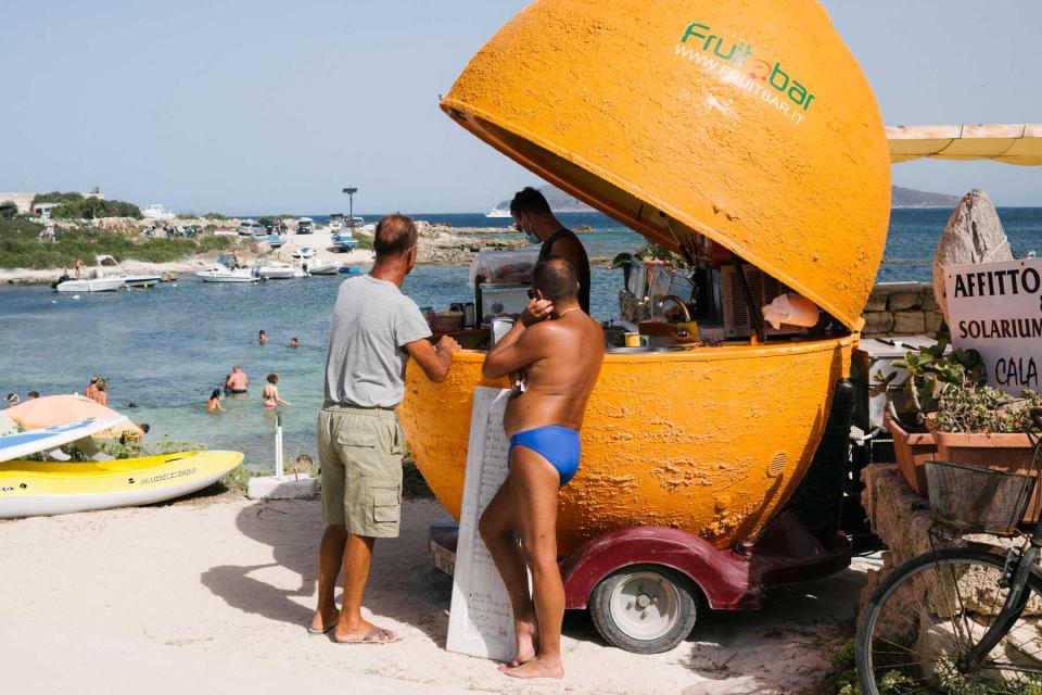 Tanned men standing at an orange-shaped juice bar on the island of Favignana