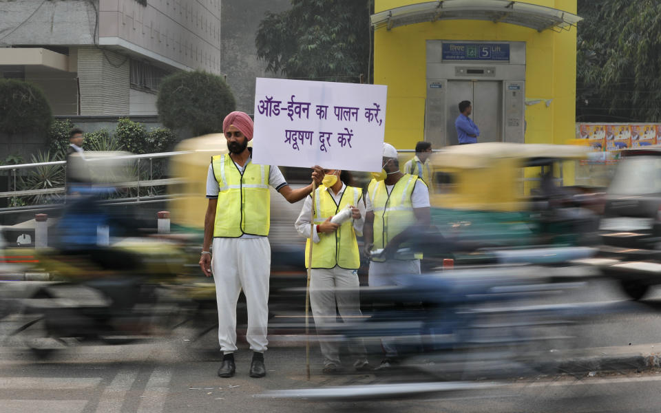 Volunteers wear pollution masks as they stand at a busy crossing with the banner saying obey odd and even, remove pollution, in New Delhi, India, Monday, Nov. 4, 2019. Authorities in New Delhi are restricting the use of private vehicles on the roads under an "odd-even" scheme based on license plates to control vehicular pollution as the national capital continues to gasp under toxic smog. (AP Photo/Manish Swarup)