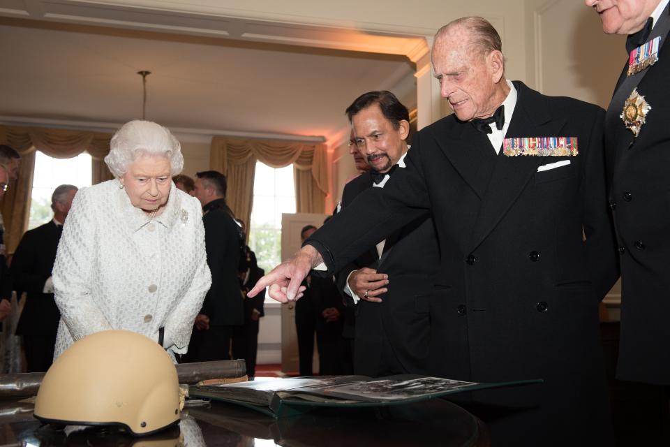 <p>The Queen and Philip, alongside the Sultan of Brunei Hassanal Bolkiah, look at the damaged helmet worn by Corporal Tuljung Gurung of the First Royal Gurkha Regiment during the Gurkha 200 pageant in the grounds of the Royal Hospital Chelsea in London on June 9, 2015. (LEON NEAL/AFP via Getty Images)</p> 