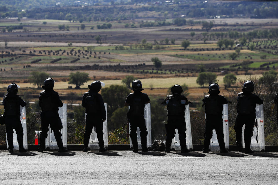 In this Feb. 6, 2020 photo, state police stand guard along the road leading into Uruapan, Michoacan state, Mexico. Uruapan, a city of about 340,000 people, is in Mexico's avocado belt, where violence has reached shocking proportions. In Uruapan, cartels are battling for territory and reports of killings are common, such as the gun massacre last week of three young boys, a teenager and five others at an arcade in what had been a relatively quiet neighborhood. (AP Photo/Marco Ugarte)