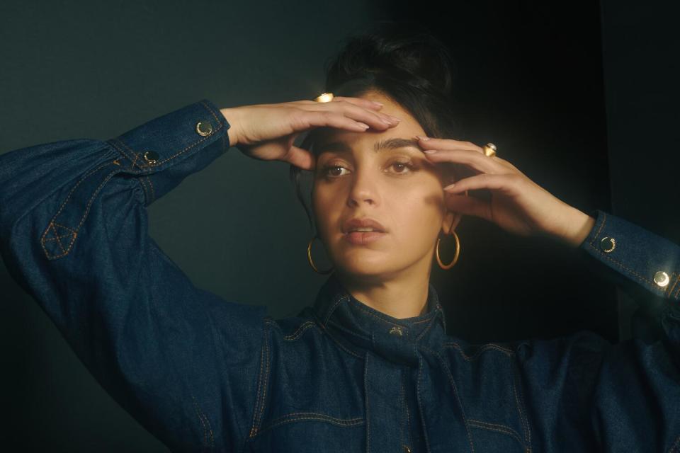 A woman holds her head and looks of camera.