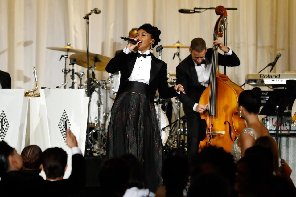 A woman on stage sings in a microphone with a viola player in front of a crowd.