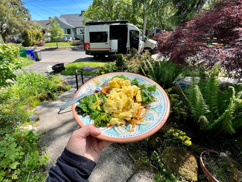 writer holding breakfast plate of eggs and greens in front of van